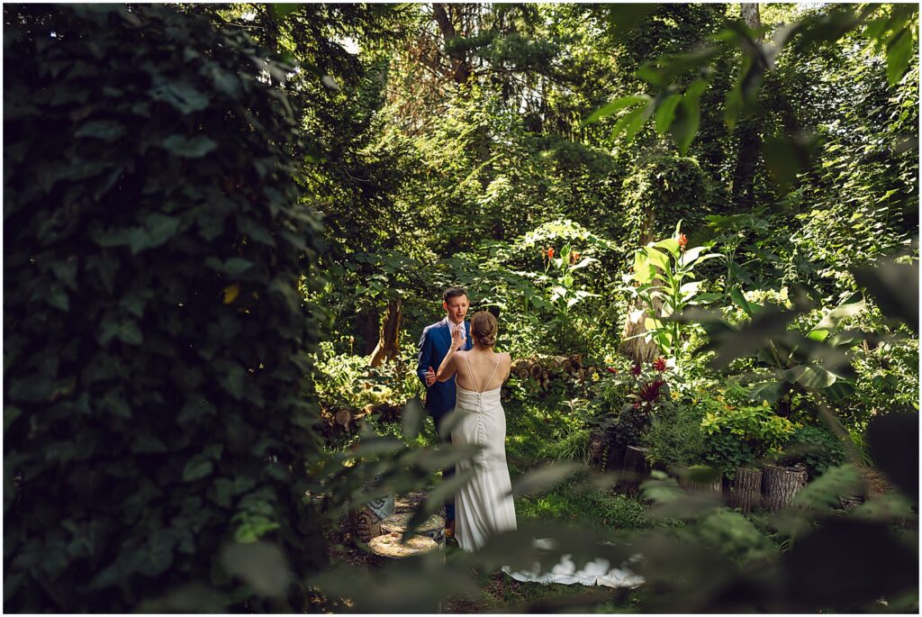 A photographer photographs a bride and groom over a bush in the Duke Sculpture Garden at Dixon Mansion.