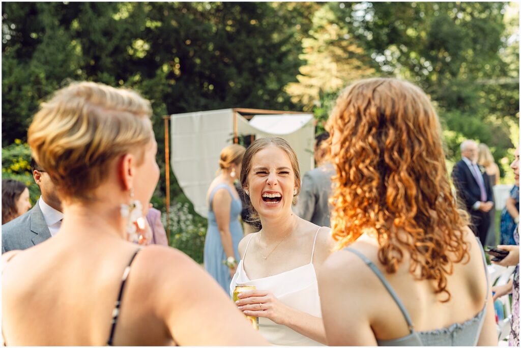 A bride laughs while she talks with friends before her outdoor wedding ceremony.