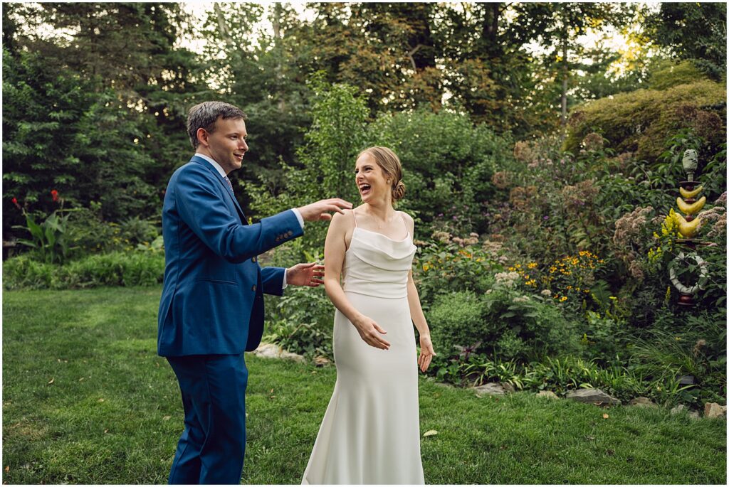 A bride and groom laugh as they walk through a garden.