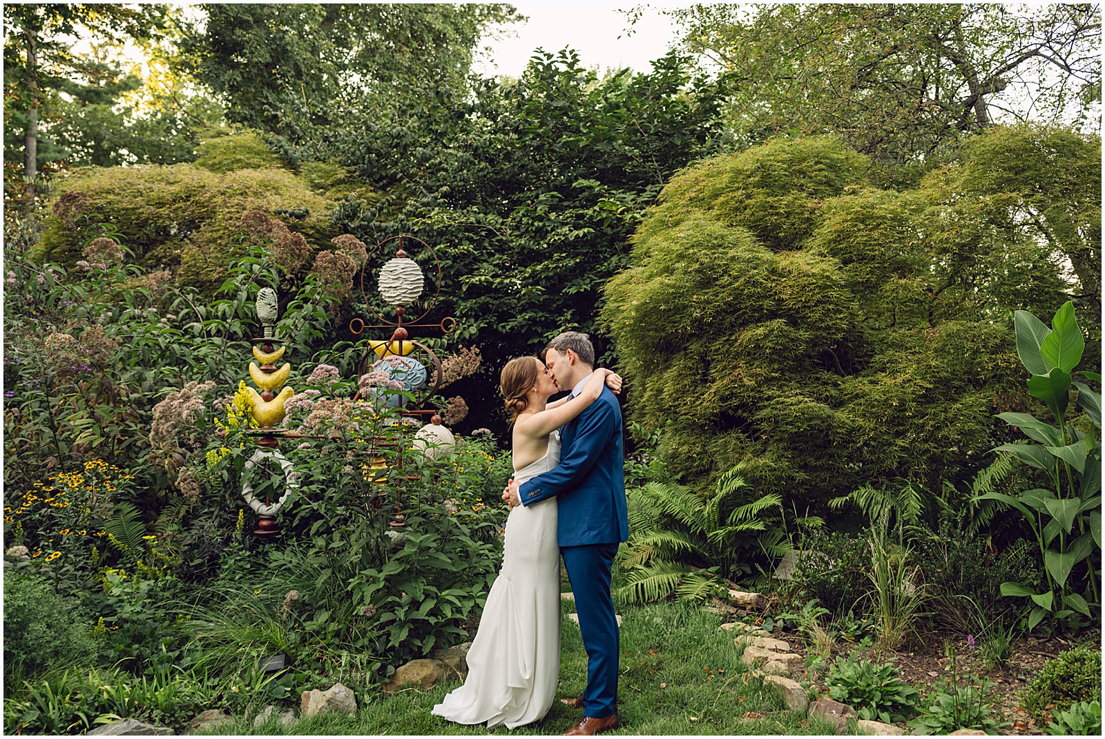 A bride and groom kiss beside some flowers in the Duke Sculpture Garden at Dixon Mansion.