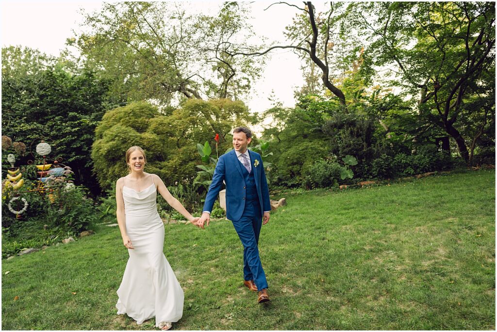 A bride and groom hold hands as they walk across a lawn.