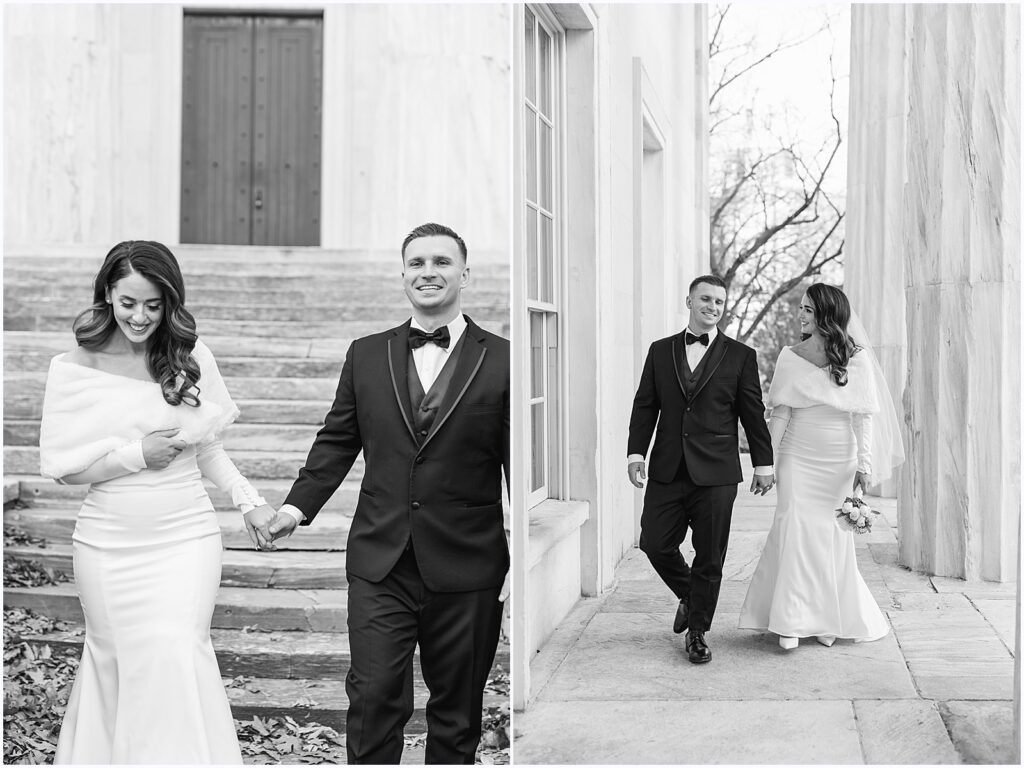 A bride and groom hold hands and walk down a path lined with pillars.