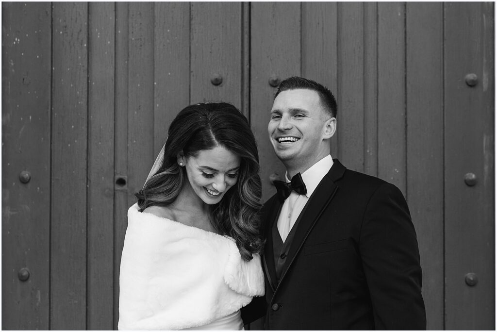 A bride and groom stand laughing in a candid wedding photo.