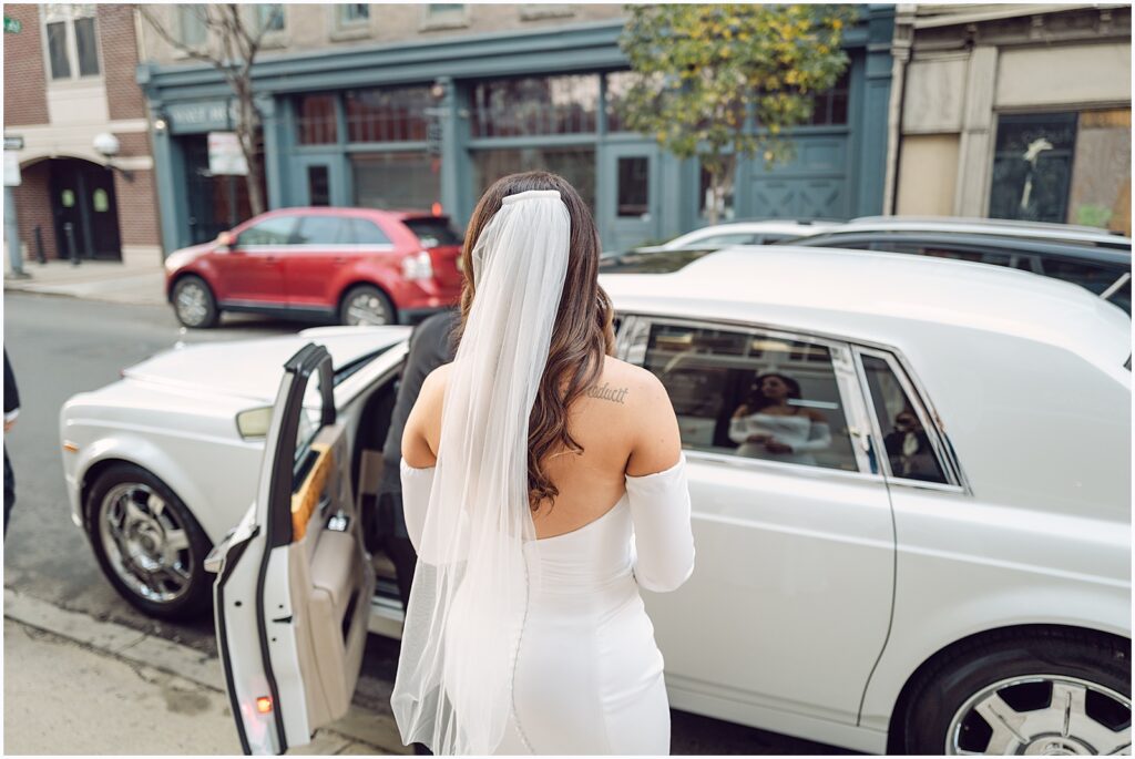 A driver opens the door of a vintage car for a bride at a winter wedding.