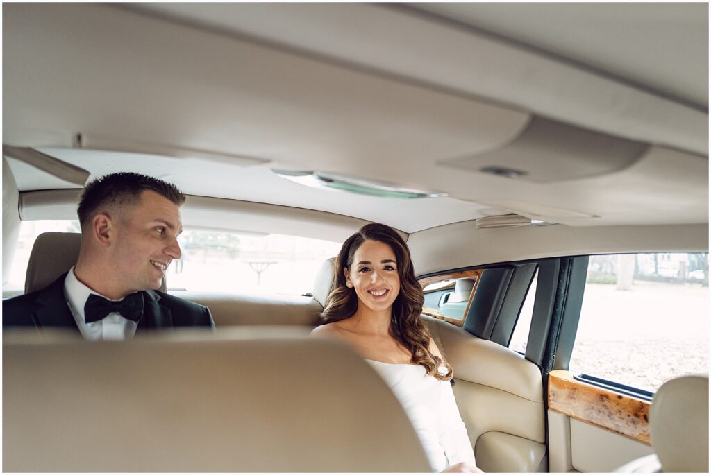 A bride smiles at a Philadelphia wedding photographer from the backseat of a car.