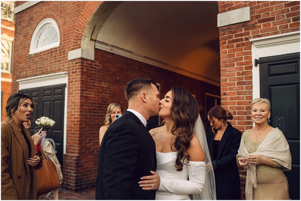 A bride and groom kiss while their family looks on at a Philadelphia micro wedding.