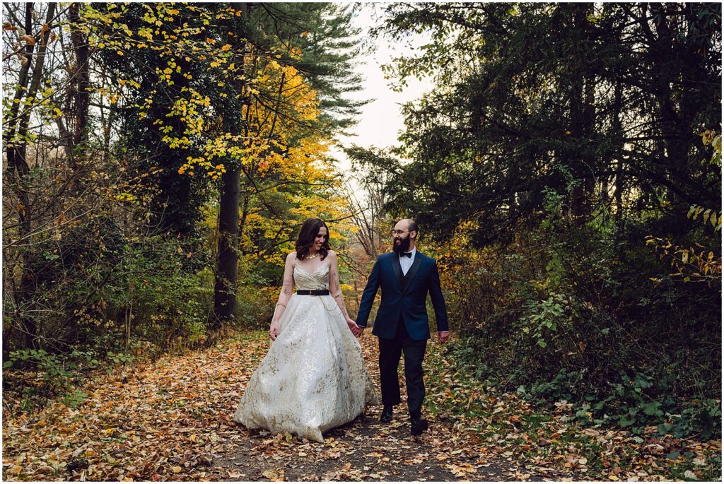 A bride and groom hold hands and walk down a path at their fall wedding.