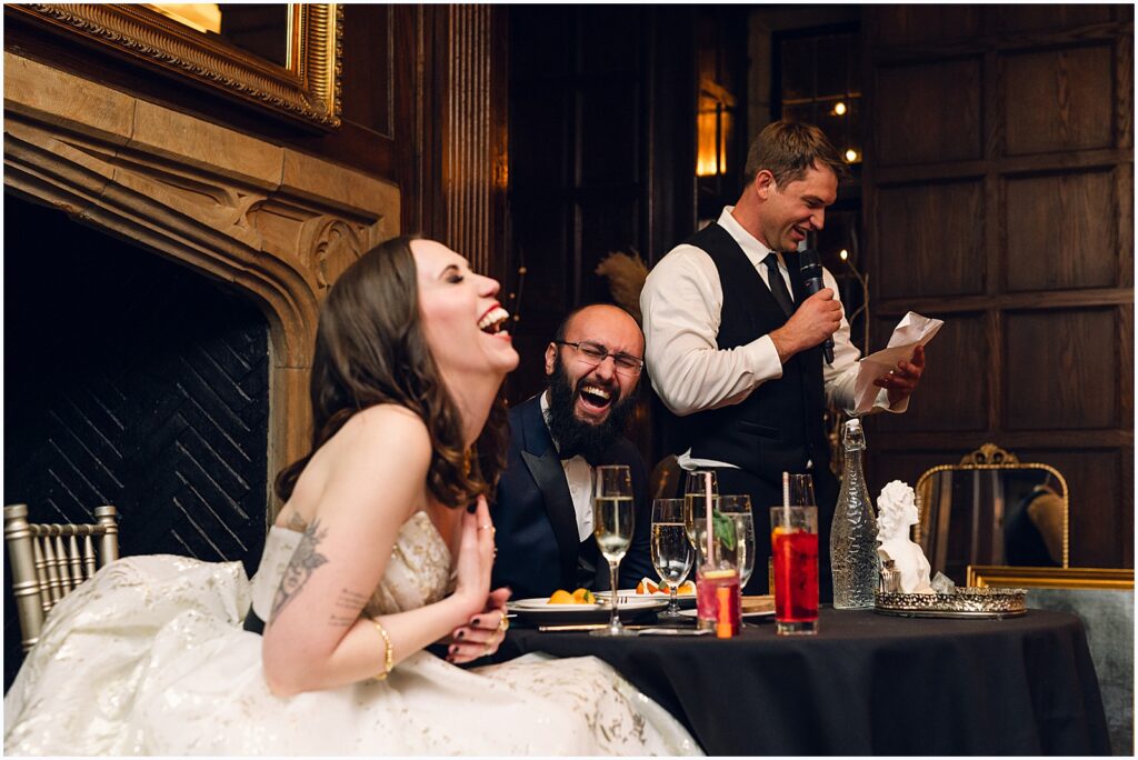 A bride and groom laugh during a speech in a candid wedding photo.