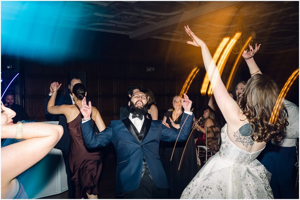A bride and groom throw up their arms on the dance floor.