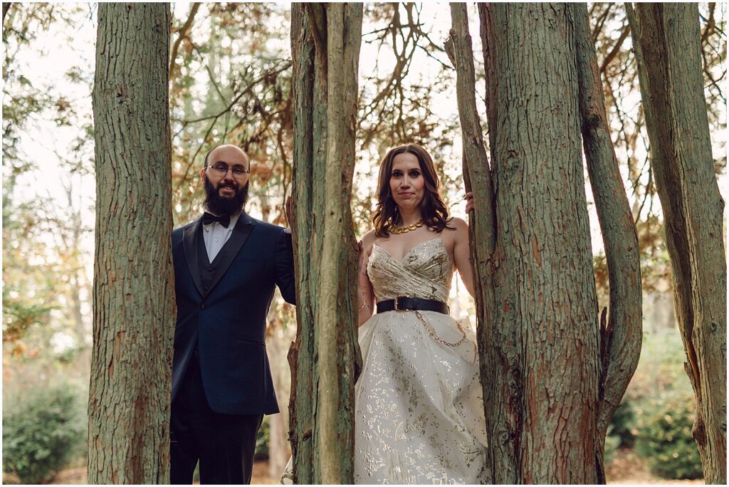 A bride and groom pose between tress for creative wedding portraits.