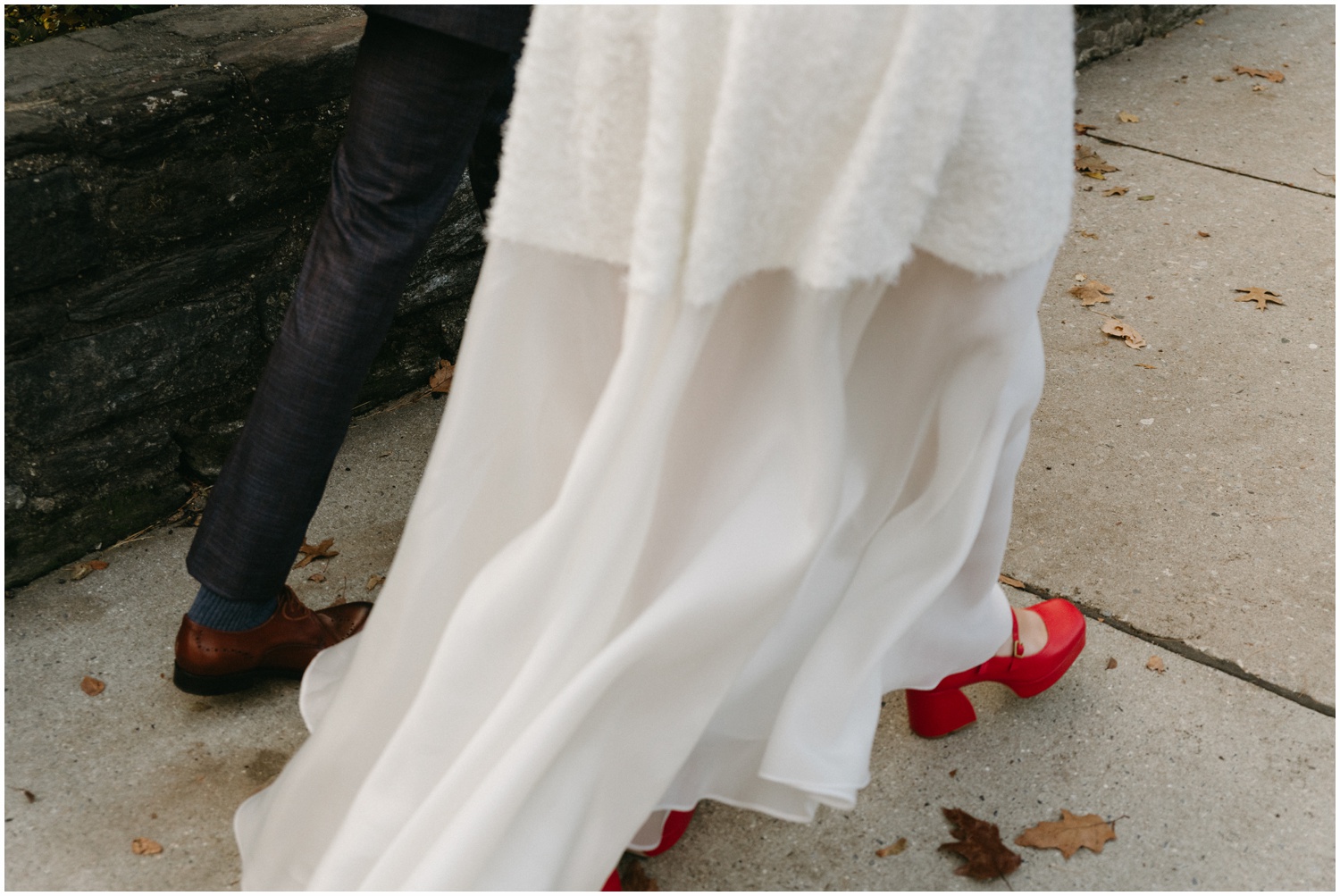 A bride in red wedding shoes walks down a Philadelphia sidewalk with a groom.