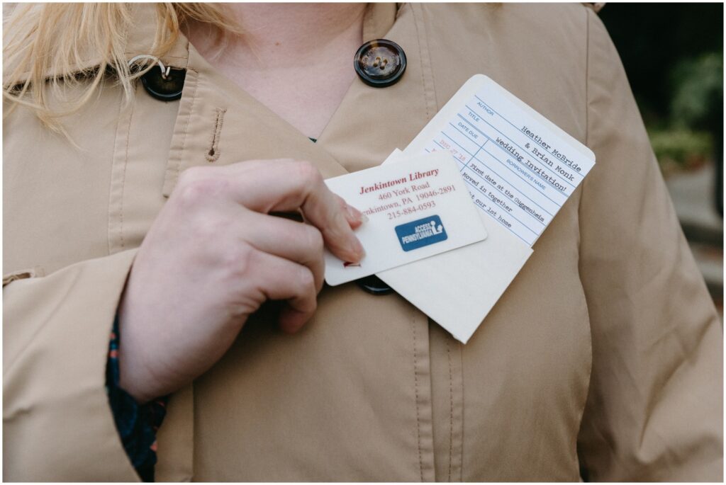 A wedding guest holds up a library card beside a unique wedding invitation.