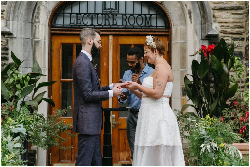 A bride places a wedding ring on a groom's finger during a small wedding ceremony.