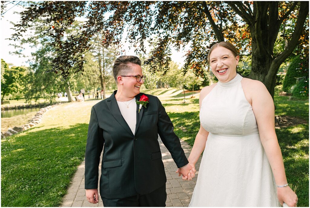 Two brides hold hands and smile at a Philadelphia wedding photographer.