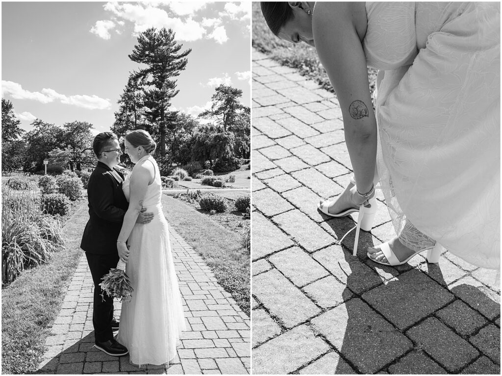 A bride leans down to fasten her white wedding shoe on a brick path.