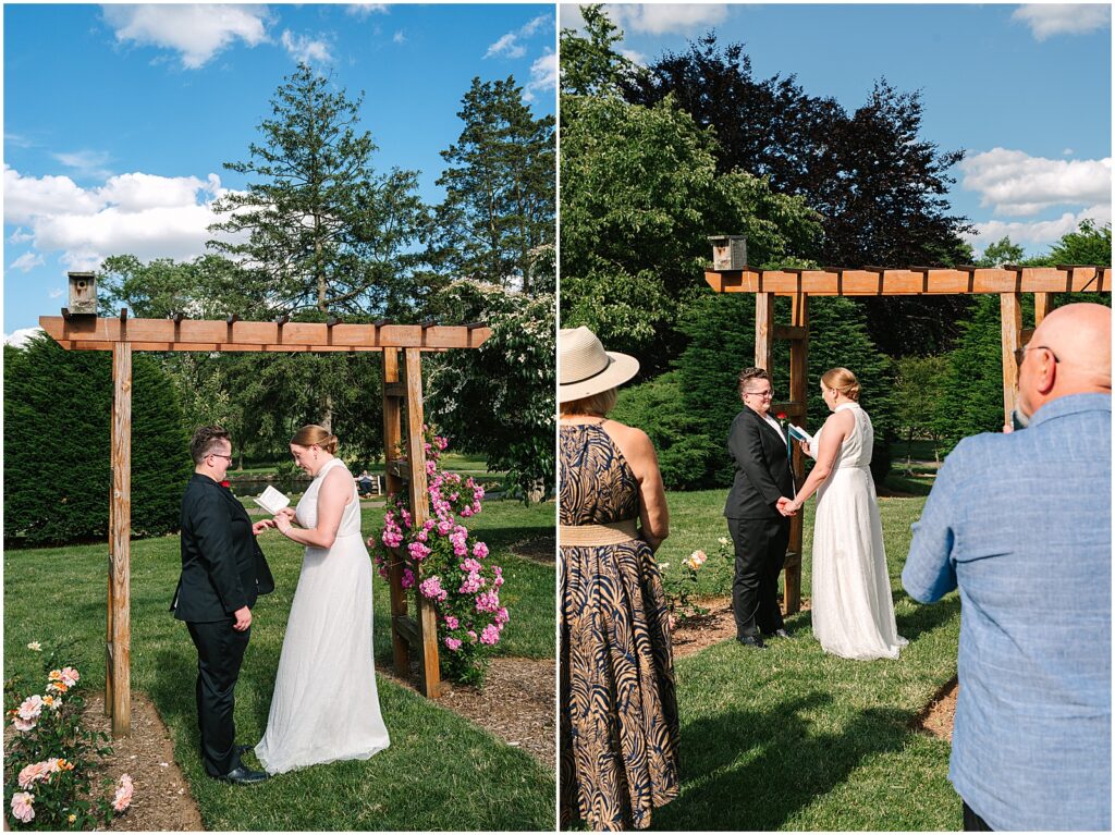 Two brides hold hands beneath a trellis during a Malcolm Gross Rose Garden wedding.