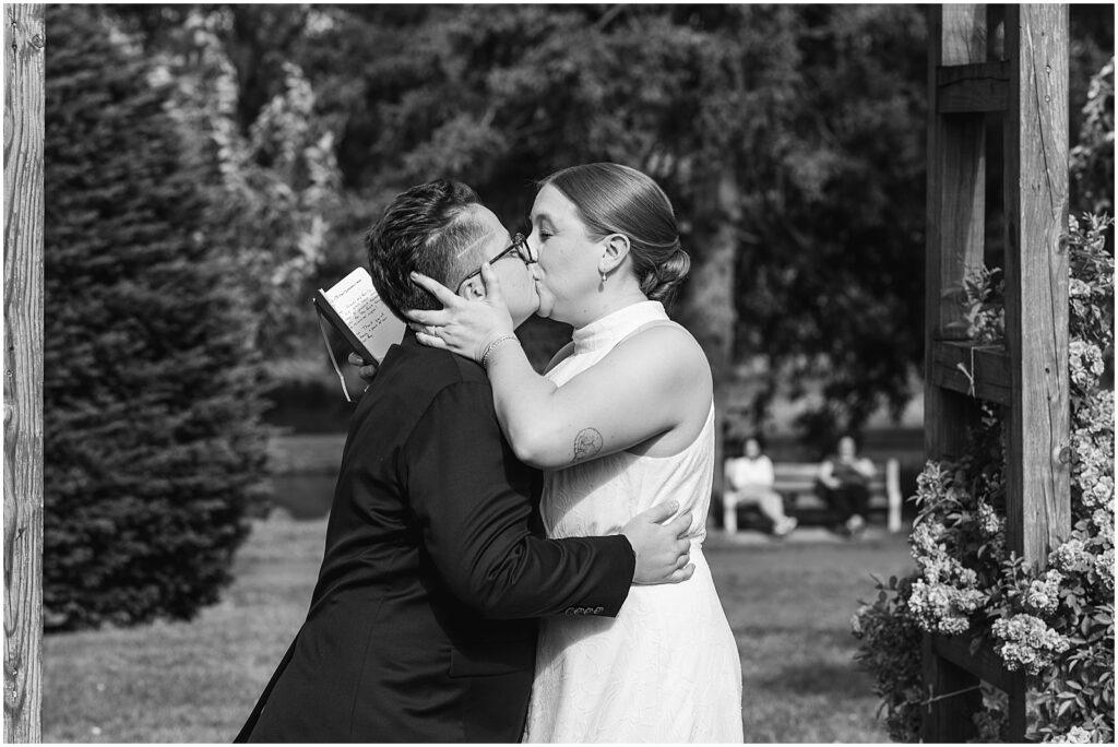 Two brides kiss at the end of their summer wedding ceremony.