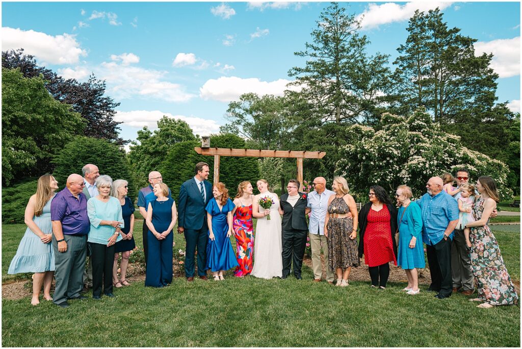 Two brides pose with their guests in front of a garden trellis.