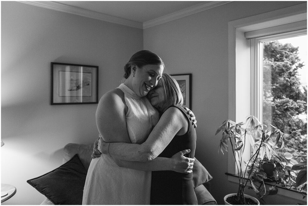 A bride hugs her mother in her living room.