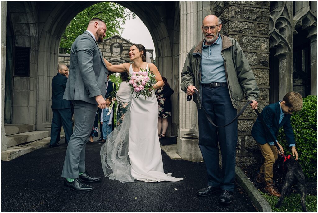 A bride pats a groom's shoulder while family members walk around them.