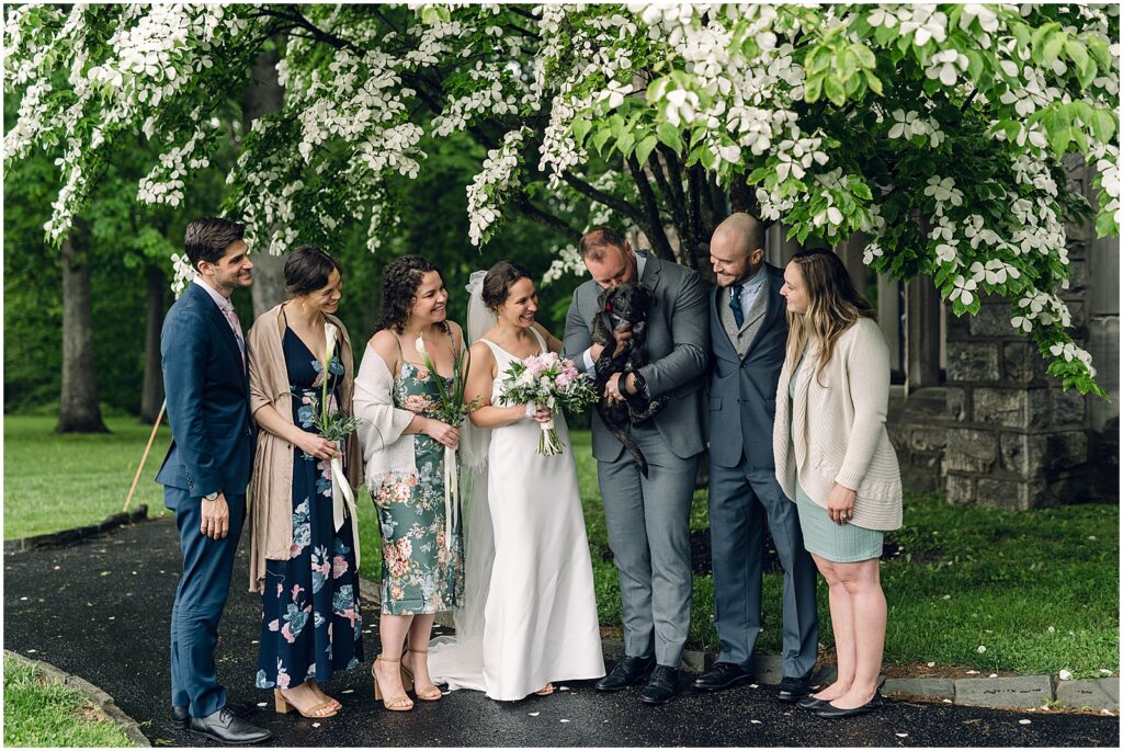 A bride and groom pose with their wedding party under a flowering tree.