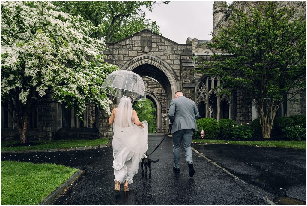 A bride carrying a clear umbrella and a groom walk away from a Philadelphia wedding photographer.