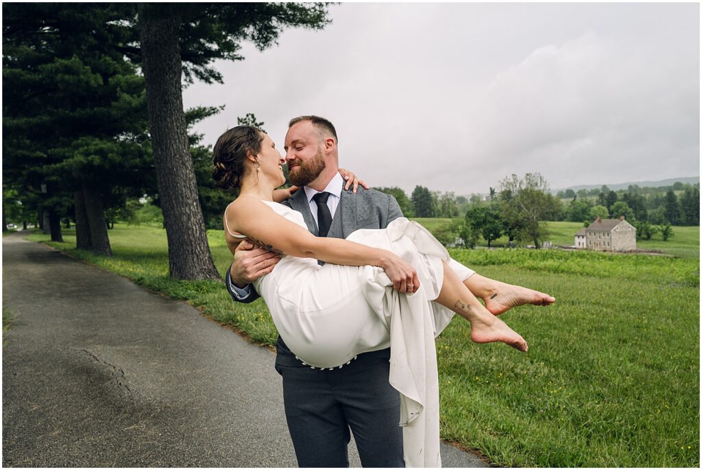 A groom carries a bride down a path outside their Philadelphia wedding ceremony venue.