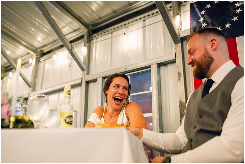 A bride and groom laugh during a wedding speech at a unique wedding reception venue.