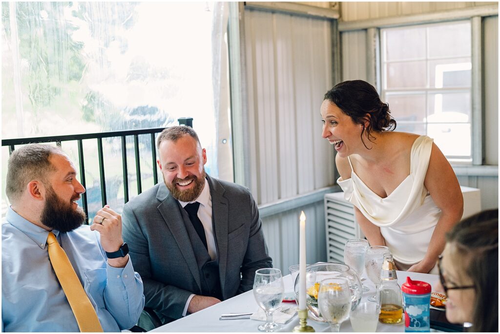 A bride leans over a table to talk to wedding guests.