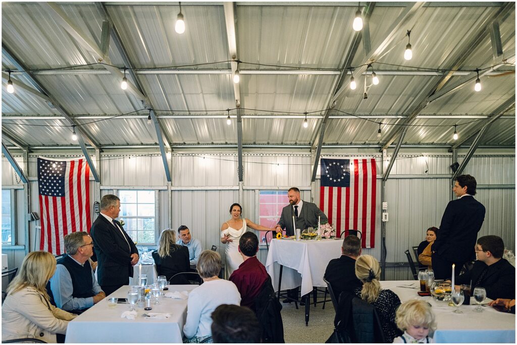 A bride and groom stand to give a speech from their sweetheart table.