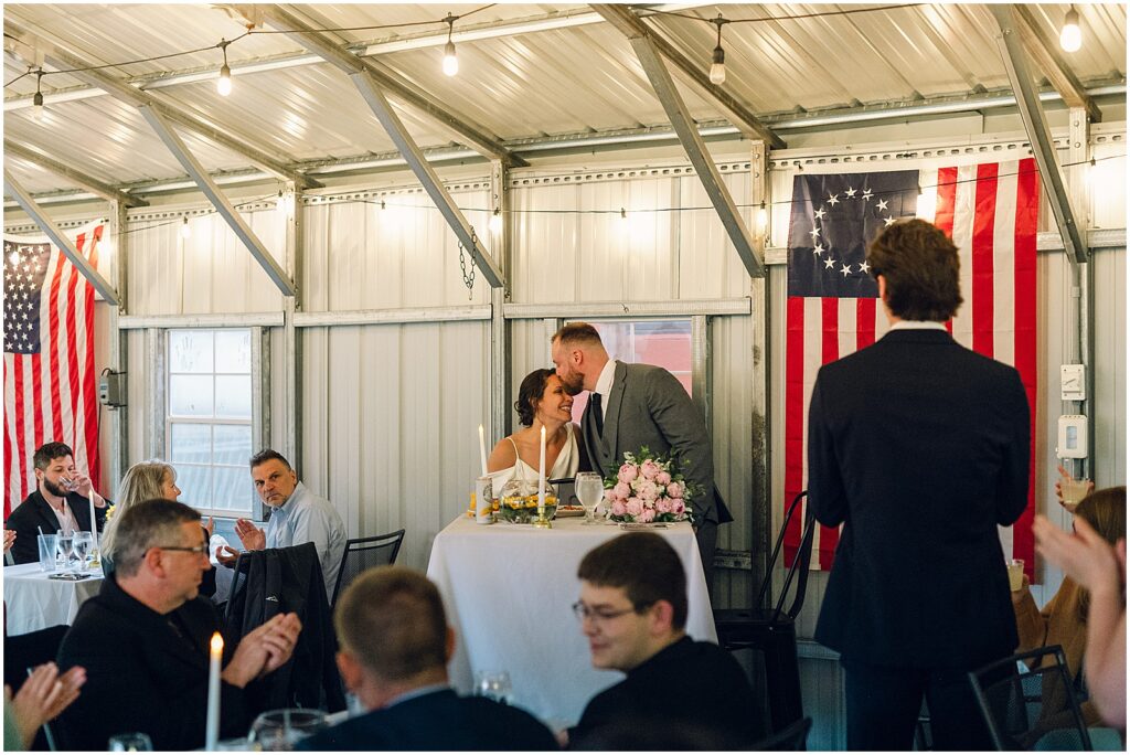 A groom kisses a bride's forehead in a diner.