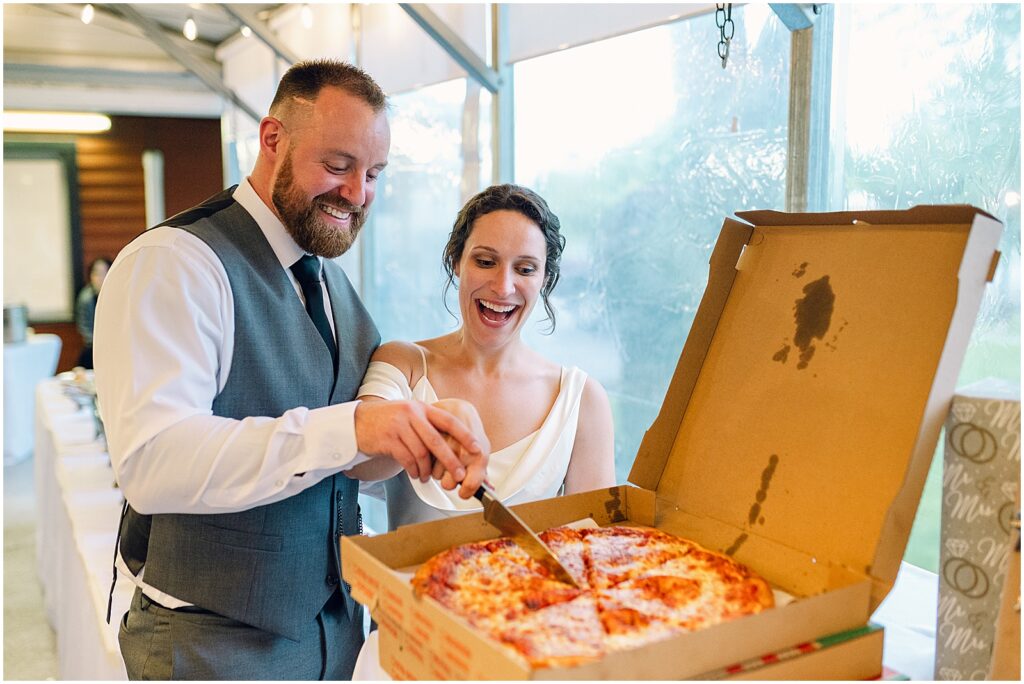 A bride and groom cut into a large pizza.