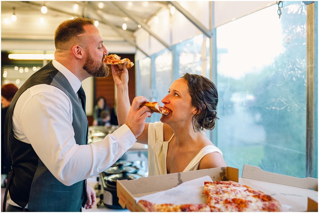 A bride and groom feed each other pizza in a unique wedding reception venue.