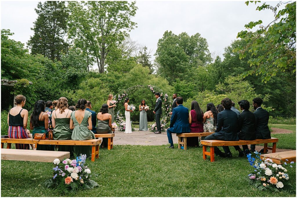 Guests sit on wooden benches to watch a summer wedding ceremony at Bowman's Hill Wildflower Preserve.