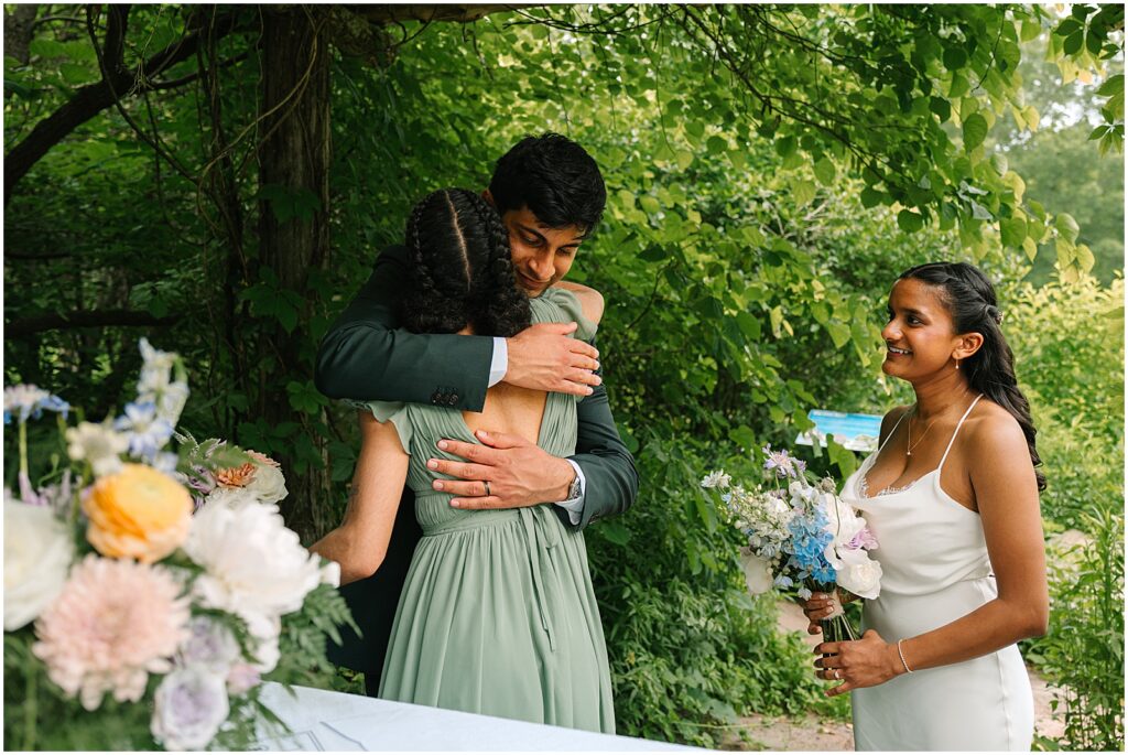 A bridesmaid hugs a groom after a marriage license signing.