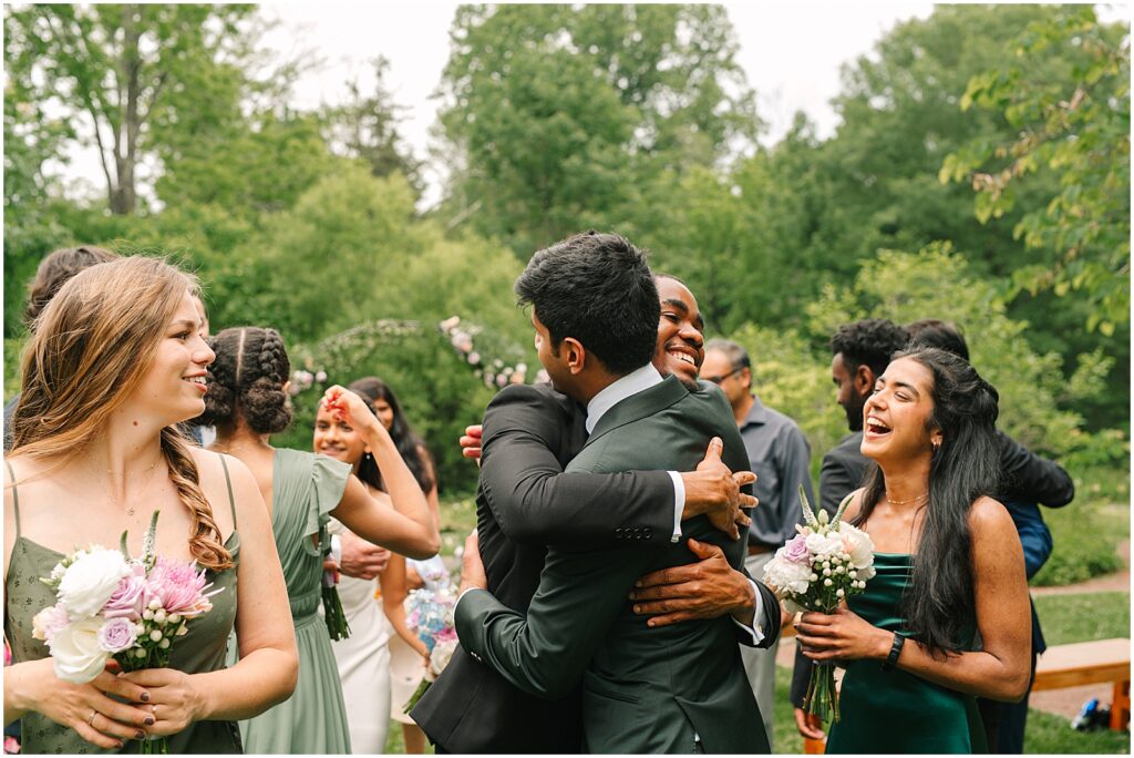 A groom hugs a groomsman after his summer wedding ceremony.