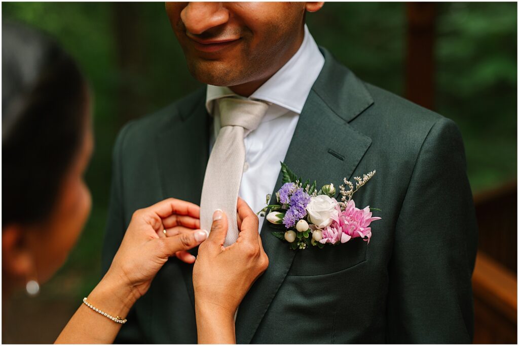 A groom smiles as a bride straightens his tie.