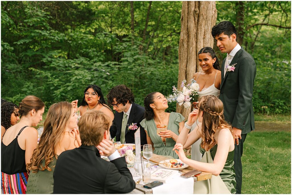 A bride and groom stand beside a wedding reception table talking to guests at Bowman's Hill Wildflower Preserve.