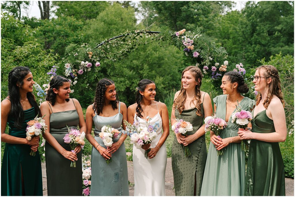 A bride poses with her bridesmaids in front of a wedding arch at Bowman's Hill Wildflower Preserve.