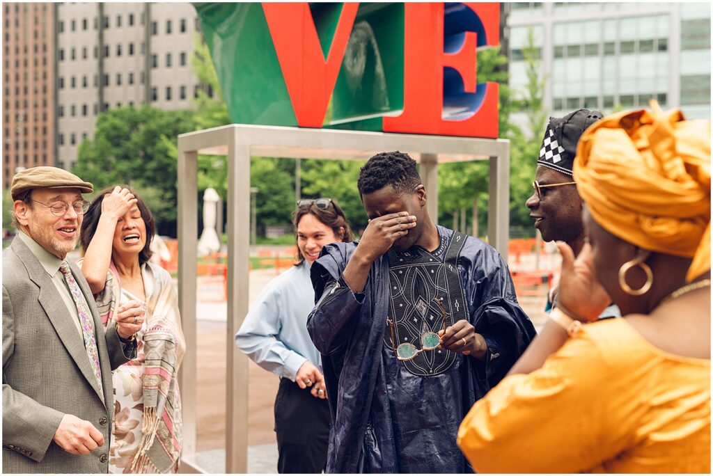 A groom wipes away tears in front of the LOVE sculpture at Love Park Philly.