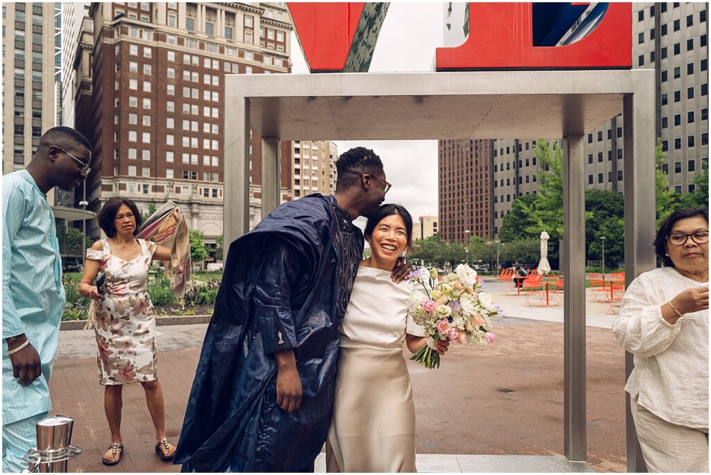 A bride smiles at a Philadelphia wedding photographer as a groom kisses her forehead.