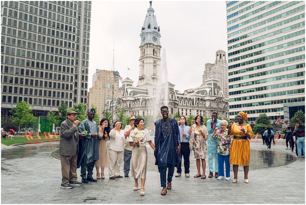 A bride and groom walk through Center City Philadelphia with City Hall behind them.