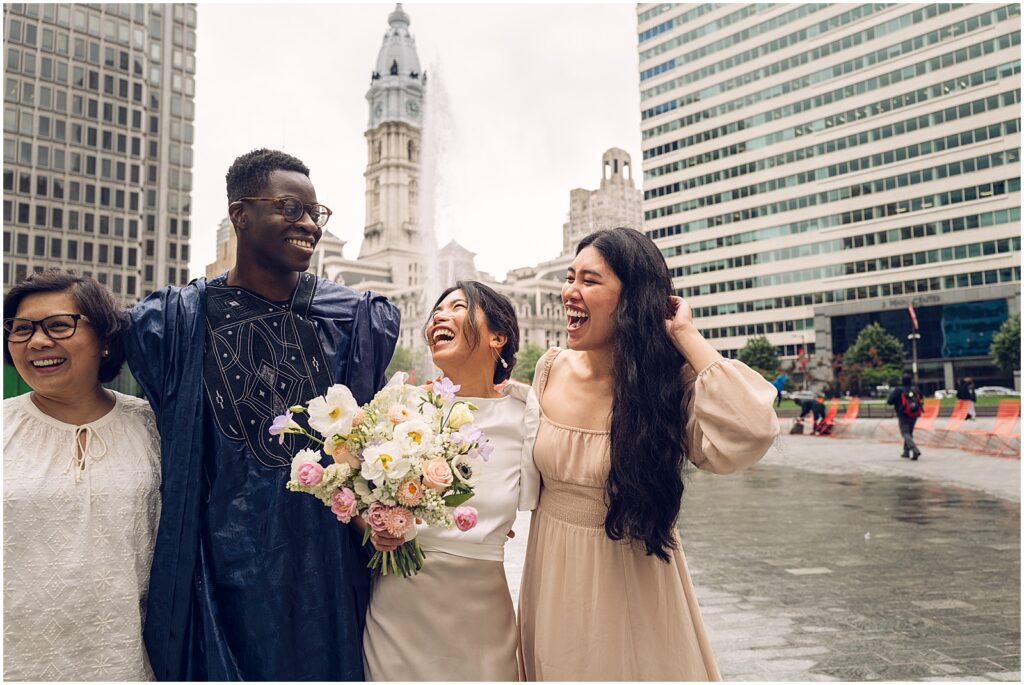 A bride and groom laugh with family members as they pose for wedding photos.