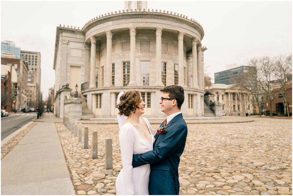 A bride and groom smile at each other on a Philadelphia street.