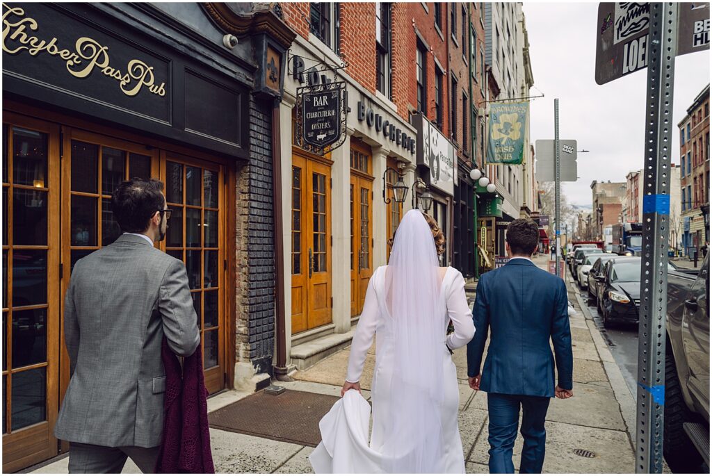 A bride and groom hold hands and walk down a sidewalk towards Royal Boucherie.