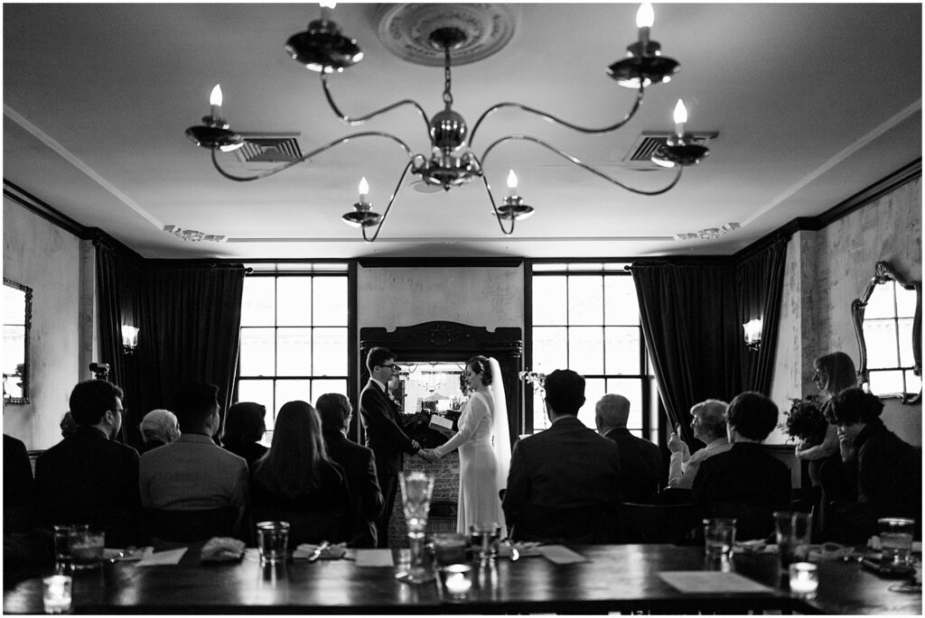 A bride and groom hold hands in front of a fireplace during a Royal Boucherie wedding.