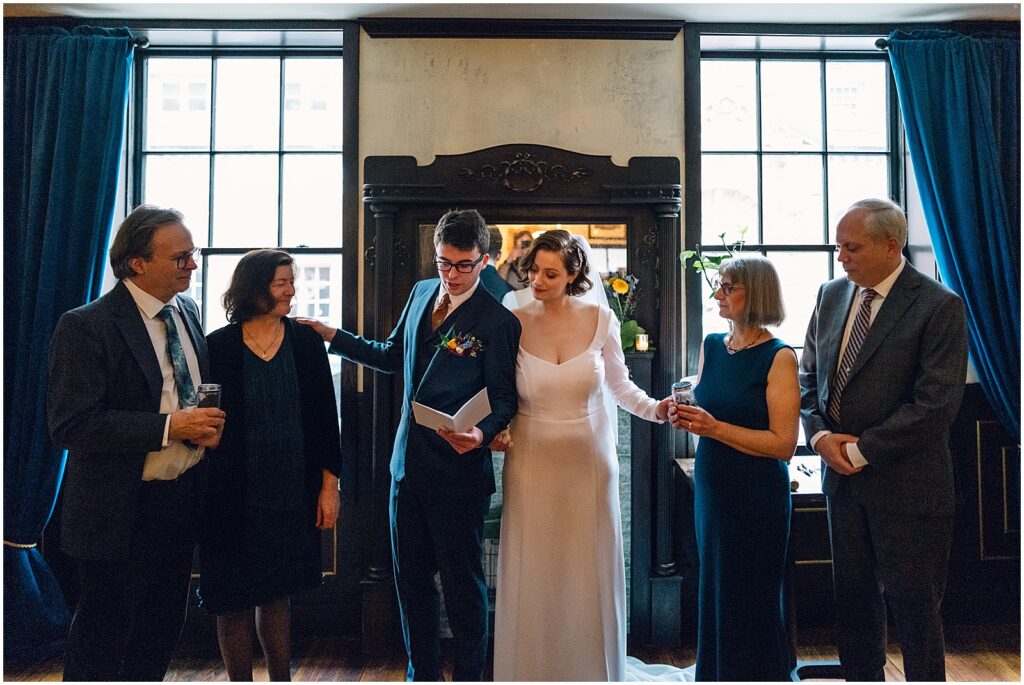 A couple's parents stand on either side of them during a wedding ceremony.