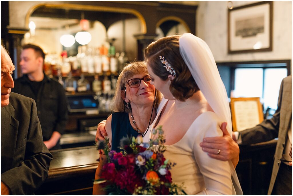 A bride's mother hugs her beside a bar.