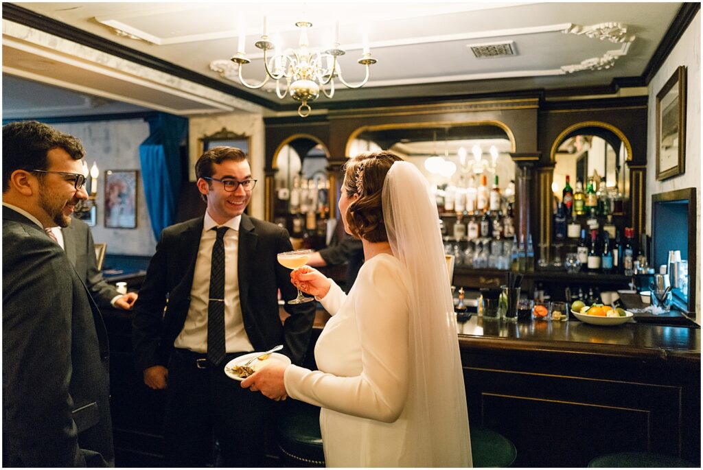 A bride and groom drink cocktails beside a bar.