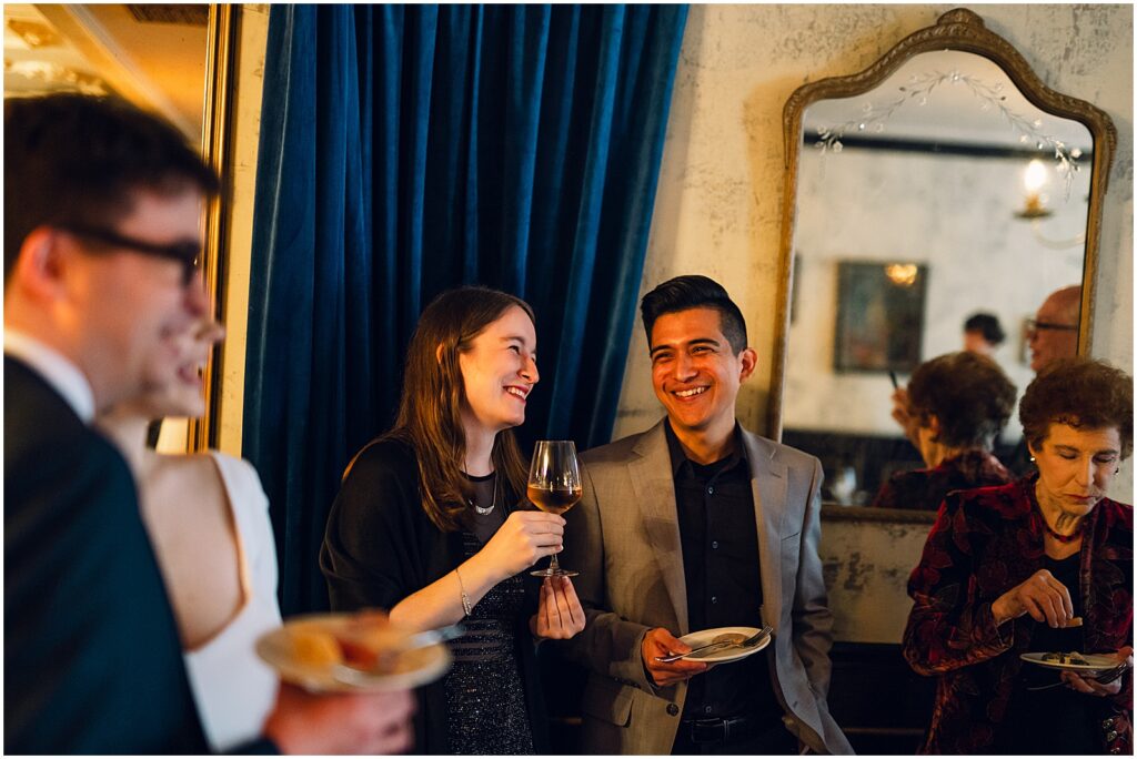 Wedding guests stand in a circle laughing.